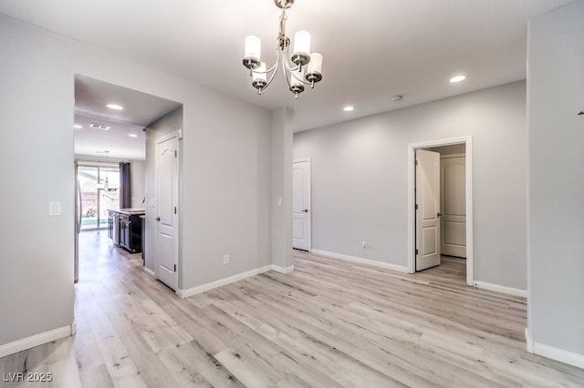 empty room with a notable chandelier and light hardwood / wood-style floors