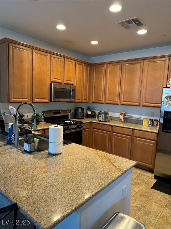 kitchen with appliances with stainless steel finishes, light tile patterned floors, and light stone counters