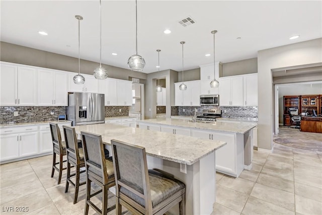 kitchen with a center island with sink, white cabinets, a kitchen breakfast bar, decorative light fixtures, and stainless steel appliances