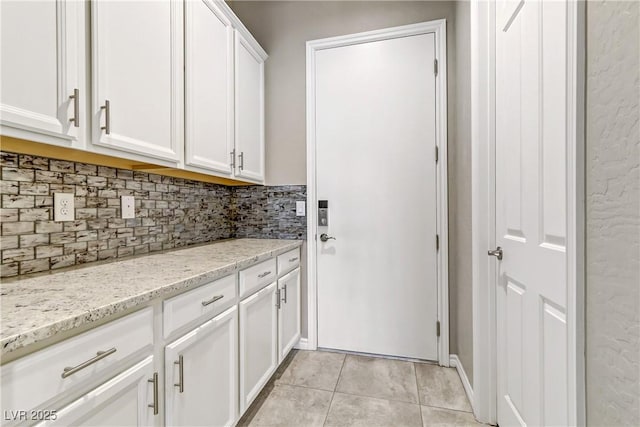 kitchen featuring decorative backsplash, light stone counters, white cabinets, and light tile patterned floors