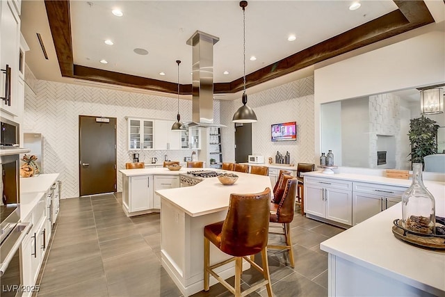 kitchen featuring a breakfast bar, a tray ceiling, decorative light fixtures, white cabinets, and a kitchen island