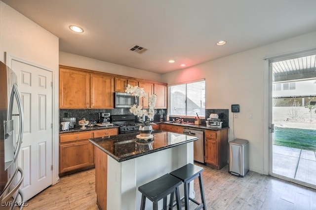 kitchen with a breakfast bar, dark stone counters, sink, light wood-type flooring, and appliances with stainless steel finishes