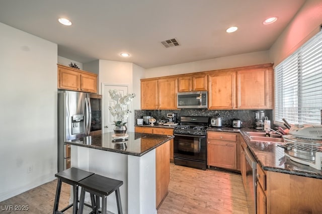 kitchen featuring light wood-type flooring, stainless steel appliances, sink, dark stone countertops, and a center island