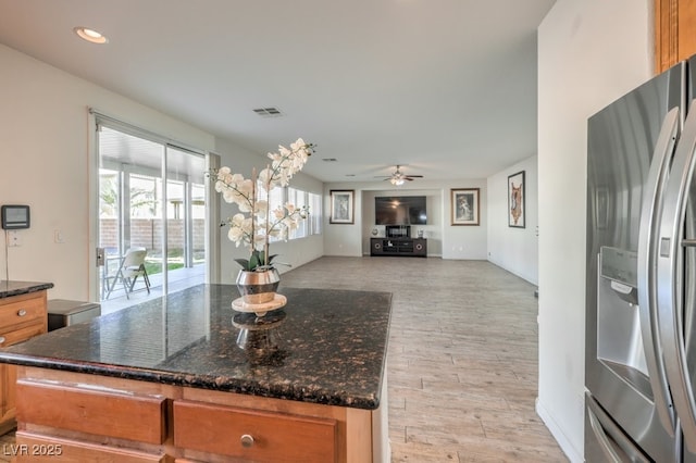 kitchen featuring stainless steel fridge, ceiling fan, and dark stone counters