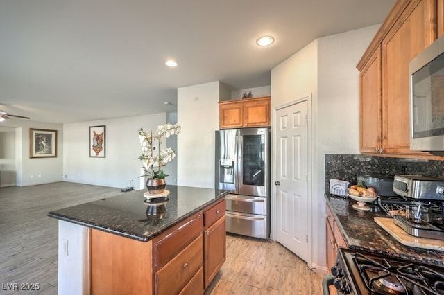 kitchen featuring a center island, dark stone counters, ceiling fan, appliances with stainless steel finishes, and tasteful backsplash