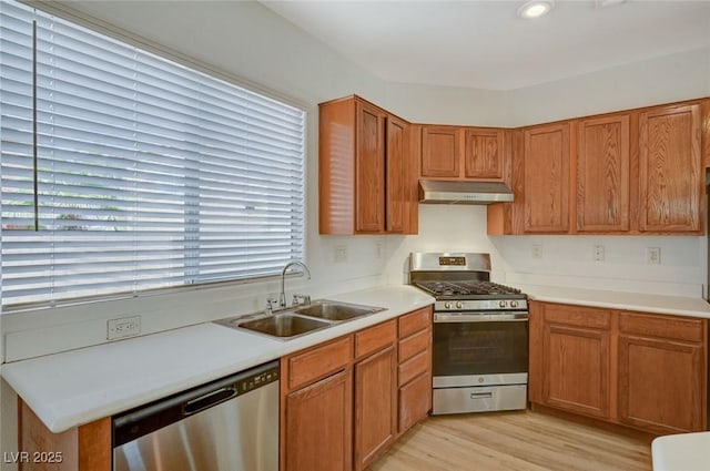 kitchen with light wood-style flooring, under cabinet range hood, a sink, appliances with stainless steel finishes, and light countertops