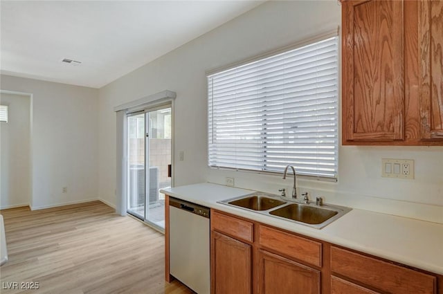 kitchen featuring stainless steel dishwasher, light countertops, light wood-type flooring, and a sink