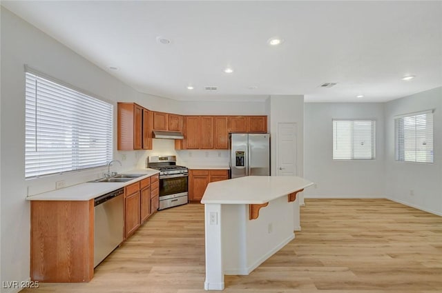 kitchen with under cabinet range hood, a sink, a kitchen island, stainless steel appliances, and light wood-style floors