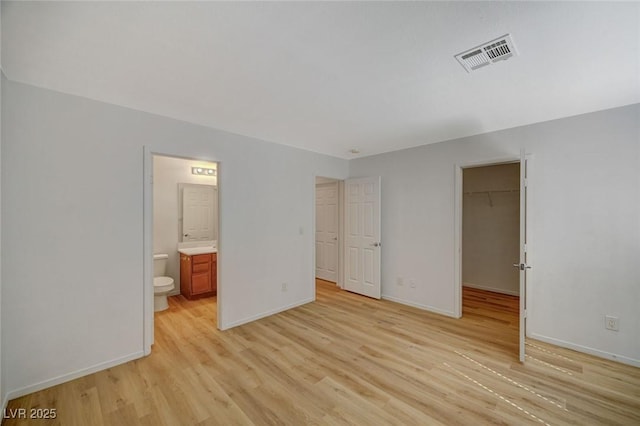 unfurnished bedroom with baseboards, visible vents, a spacious closet, ensuite bathroom, and light wood-type flooring