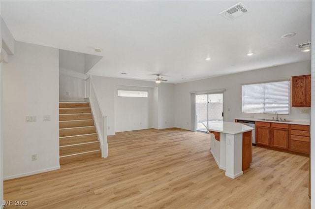 kitchen with visible vents, a sink, brown cabinetry, light wood finished floors, and dishwasher