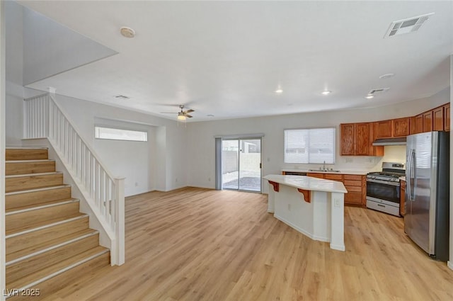 kitchen featuring visible vents, light wood-style flooring, under cabinet range hood, appliances with stainless steel finishes, and brown cabinets