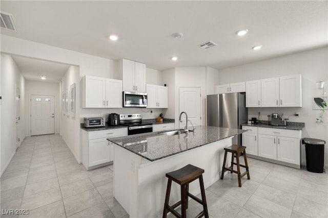 kitchen with sink, stainless steel appliances, dark stone countertops, a kitchen island with sink, and white cabinets