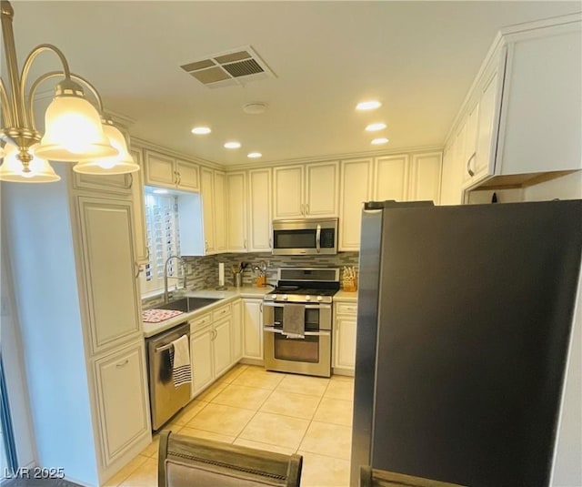 kitchen featuring appliances with stainless steel finishes, sink, light tile patterned floors, white cabinets, and hanging light fixtures