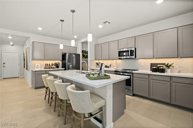 kitchen with gray cabinets, a kitchen island with sink, and appliances with stainless steel finishes