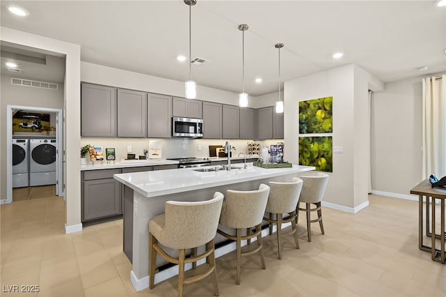 kitchen featuring washing machine and clothes dryer, gray cabinetry, sink, and hanging light fixtures