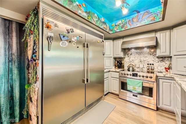 kitchen featuring backsplash, white cabinetry, wall chimney range hood, and stainless steel appliances