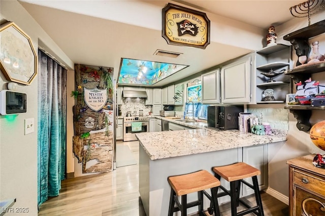 kitchen featuring stainless steel range, ventilation hood, kitchen peninsula, a breakfast bar area, and decorative backsplash