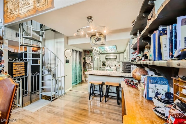 kitchen featuring wall chimney exhaust hood, tasteful backsplash, light hardwood / wood-style flooring, kitchen peninsula, and stainless steel stove