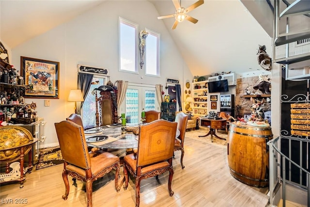 dining space with high vaulted ceiling, french doors, ceiling fan, light wood-type flooring, and a fireplace