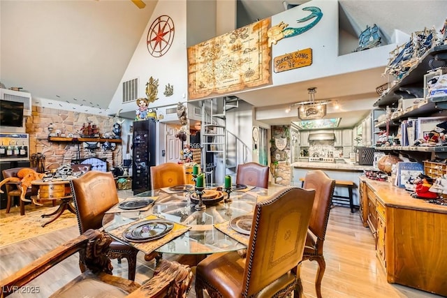 dining space with a fireplace, light hardwood / wood-style floors, and high vaulted ceiling