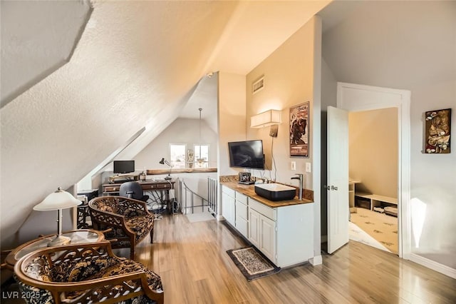 kitchen with a textured ceiling, light wood-type flooring, white cabinetry, and lofted ceiling