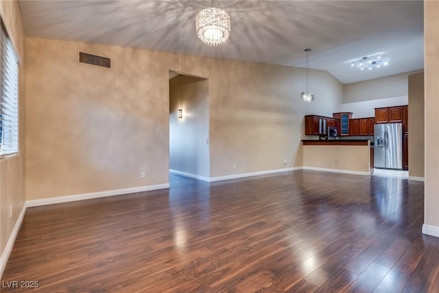 unfurnished living room with lofted ceiling, dark wood-type flooring, and an inviting chandelier