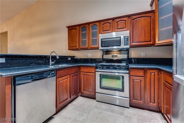 kitchen with light tile patterned floors, stainless steel appliances, dark stone counters, and sink