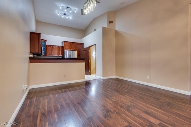 unfurnished living room with a notable chandelier, dark wood-type flooring, and a high ceiling