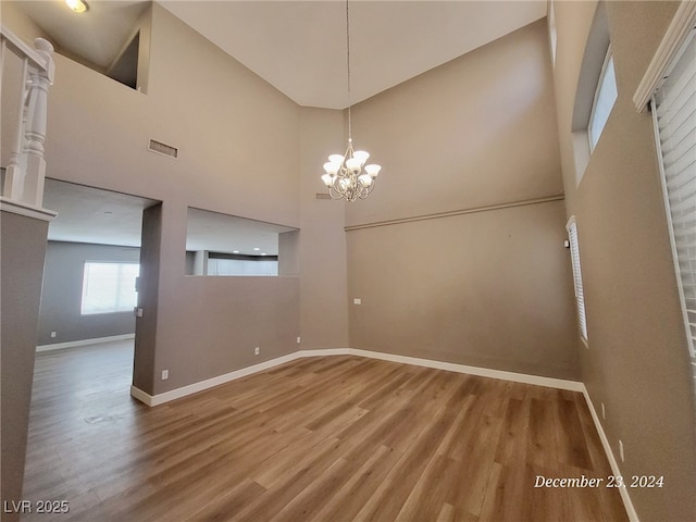 unfurnished dining area with wood-type flooring, a towering ceiling, and a notable chandelier