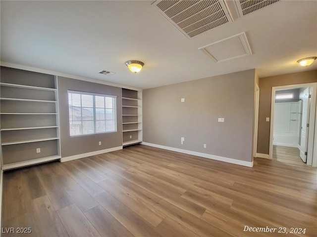 unfurnished room with built in shelves and wood-type flooring