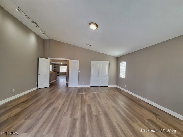 spare room featuring rail lighting, hardwood / wood-style flooring, and high vaulted ceiling