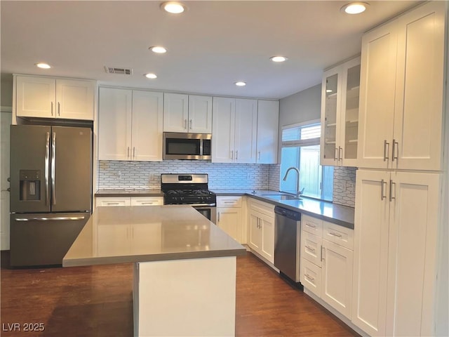 kitchen with sink, a kitchen island, tasteful backsplash, white cabinets, and appliances with stainless steel finishes