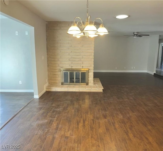 unfurnished living room featuring dark hardwood / wood-style floors, ceiling fan with notable chandelier, and a brick fireplace