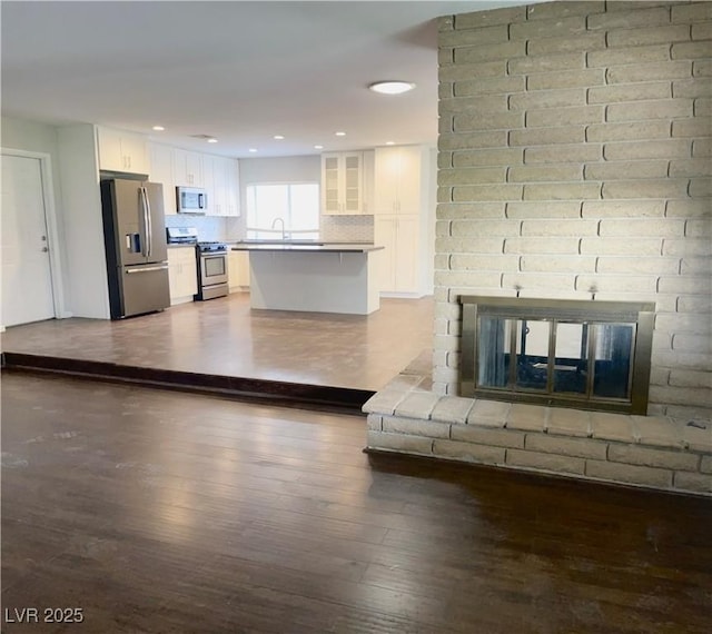 kitchen featuring dark wood-type flooring, white cabinets, a fireplace, appliances with stainless steel finishes, and a kitchen island