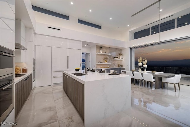 kitchen with white cabinetry, a kitchen island with sink, sink, and oven