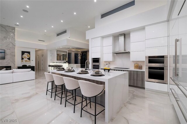 kitchen featuring white cabinets, a kitchen breakfast bar, a spacious island, and wall chimney range hood