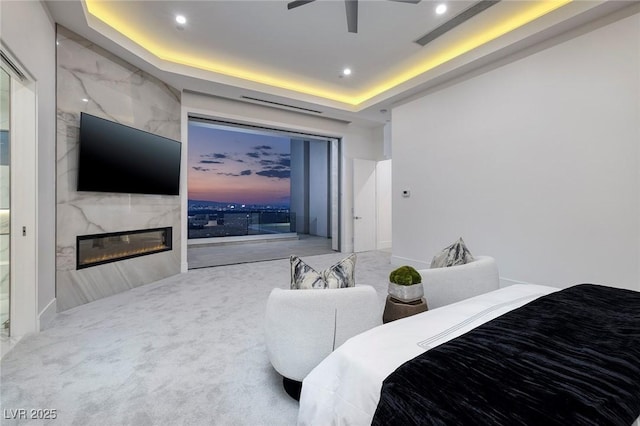 carpeted bedroom featuring a tray ceiling, ceiling fan, and a high end fireplace