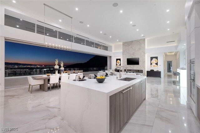 kitchen featuring white cabinets, a large island with sink, a high end fireplace, and sink