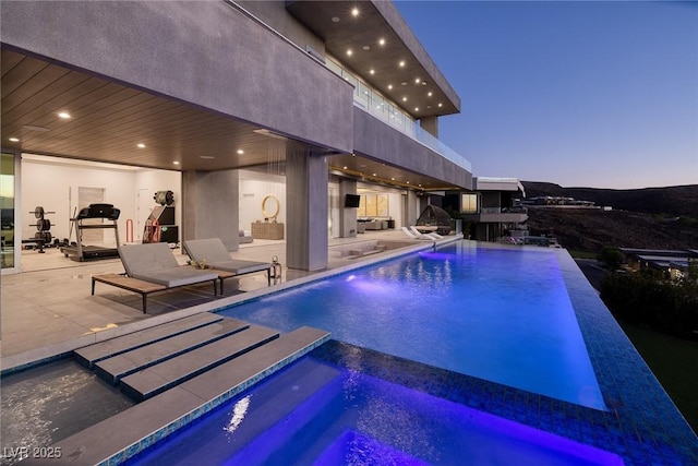 pool at dusk with a patio area and an in ground hot tub