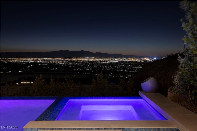 pool at night featuring an in ground hot tub and a mountain view