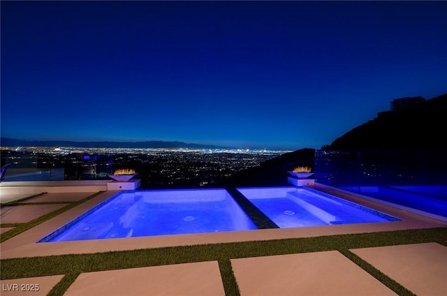 pool at twilight featuring an in ground hot tub