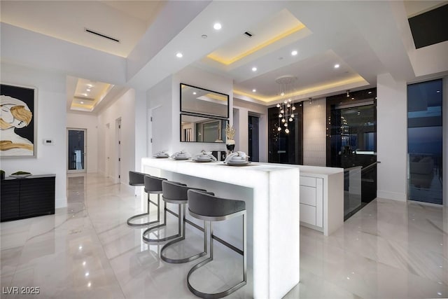 kitchen featuring a tray ceiling, kitchen peninsula, a breakfast bar, and white cabinets