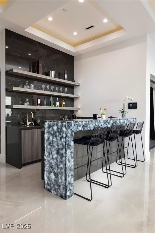 bar with dark brown cabinetry, a raised ceiling, and sink