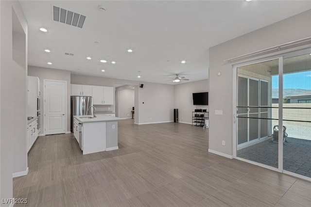 kitchen with a kitchen island with sink, ceiling fan, sink, white cabinetry, and stainless steel refrigerator