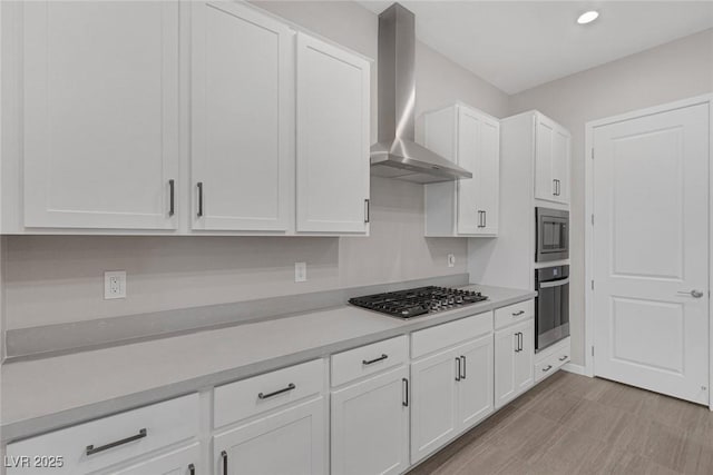 kitchen featuring white cabinetry, stainless steel appliances, wall chimney range hood, and light wood-type flooring