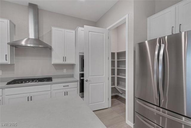 kitchen with white cabinetry, stainless steel appliances, and wall chimney range hood