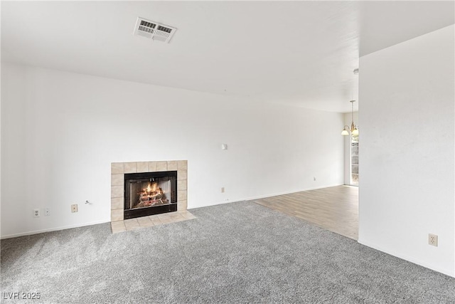 unfurnished living room featuring light colored carpet, a tile fireplace, and a chandelier