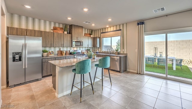 kitchen with a kitchen breakfast bar, sink, light stone countertops, appliances with stainless steel finishes, and a kitchen island