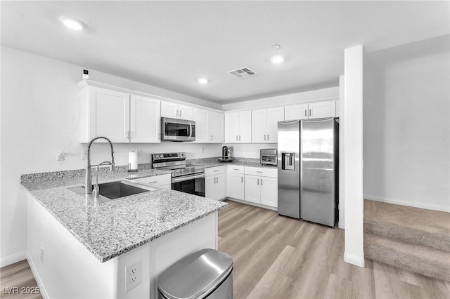 kitchen with kitchen peninsula, light stone countertops, stainless steel appliances, sink, and white cabinetry