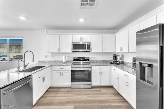 kitchen featuring white cabinets, appliances with stainless steel finishes, light stone counters, and sink